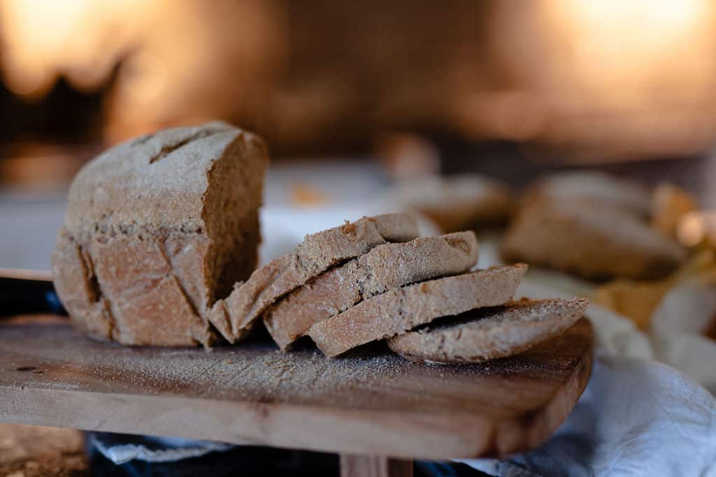 A golden, crusty loaf of fresh milled bread on a wooden table, sliced open to reveal a soft, hearty crumb—radiating warmth, freshness, and artisan quality